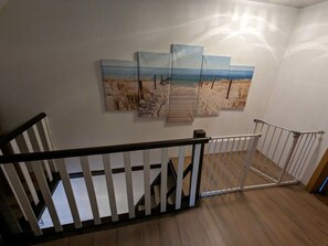 A staircase with a white railing, wooden steps, and a wall with three beach-themed paintings. - Huus Meta Modern Retreat (Krummhoern)