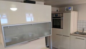 A modern kitchen with white cabinetry, a built-in oven, and a microwave. - Huus Meta Modern Retreat (Krummhoern)