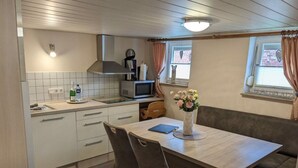 A compact kitchen with a microwave, kettle, and a small dining area with a table and chairs. - Huus Meta Modern Retreat (Krummhoern)