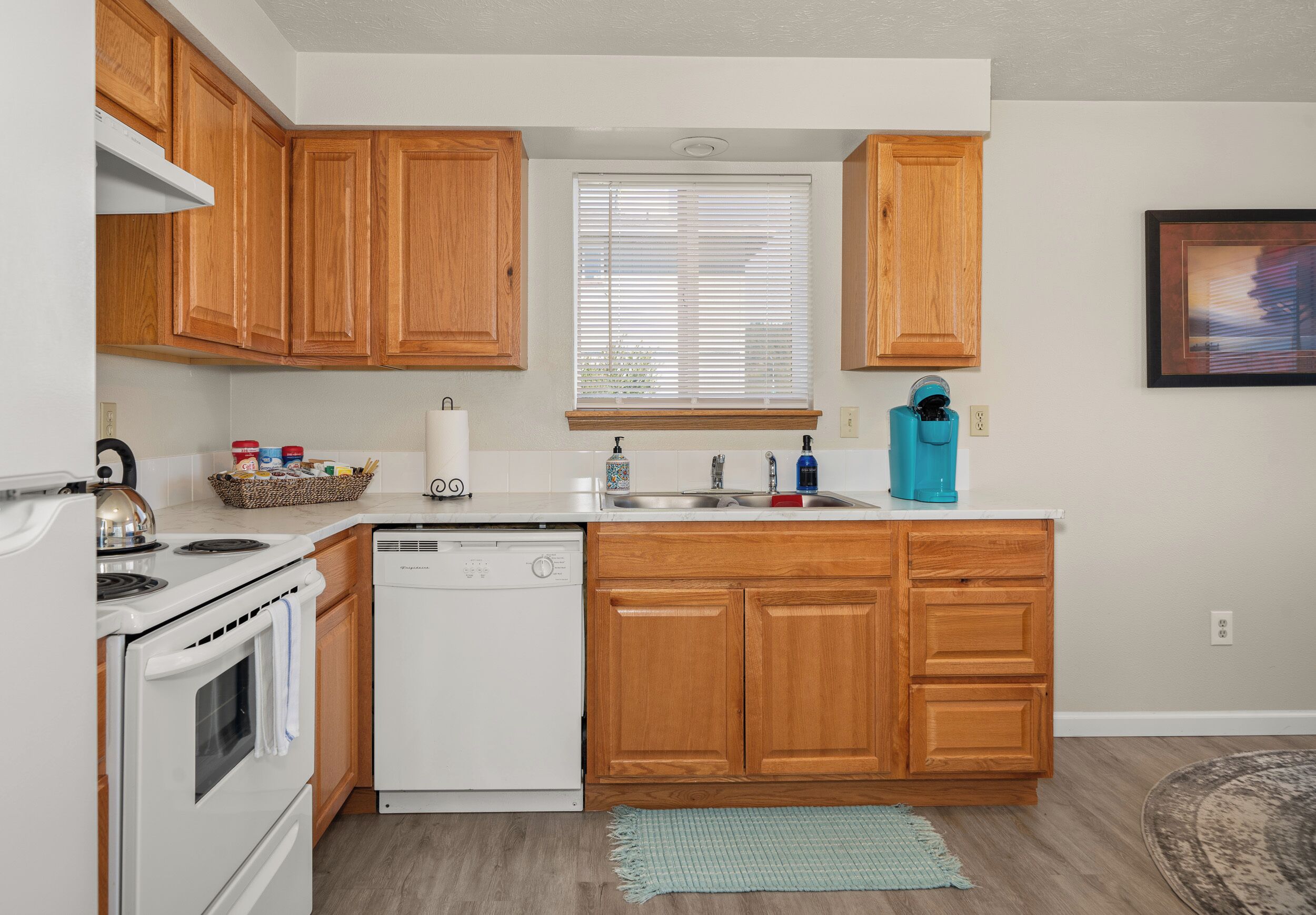 A kitchen with wooden cabinets, a white stove, a dishwasher, and a window with blinds.