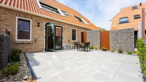 A residential building with a tiled roof, brick walls, and a paved patio area with outdoor furniture. - Luxury new Apartment on Ameland (Buren)