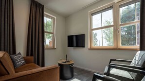 A room with two windows, a sofa, a chair, a TV, and a small round table with a candle. - Luxury new Apartment on Ameland (Buren)