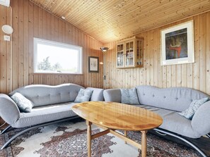 Un salon chaleureux avec un plafond en bois, un canapé gris, une table basse en bois et un tapis à motifs.
