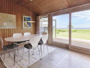 Un espace repas doté d’un plafond en bois, d’une grande fenêtre offrant une vue sur la mer et d’une carte accrochée au mur.