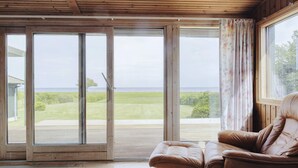 A room with a sliding glass door leading to a grassy area, a brown leather chair, and a window with curtains. - 4 Star Holiday Home in Praesto (Praesto)