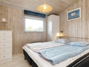 Une chambre à coucher avec un lit, une commode, une fenêtre et une lampe fixée au mur.