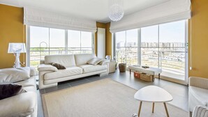 Una sala de estar moderna con un amplio ventanal, un sofá blanco, una mesita pequeña y una lámpara de pie.