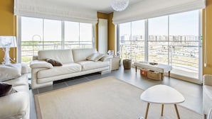 Un salón espacioso con un ventanal grande, un sofá blanco, una mesita y una lámpara decorativa.