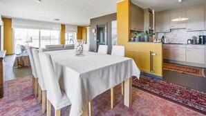 Una cocina moderna con una pared de acento amarilla, un comedor con mesa blanca y vistas a la ciudad a través de amplios ventanales.