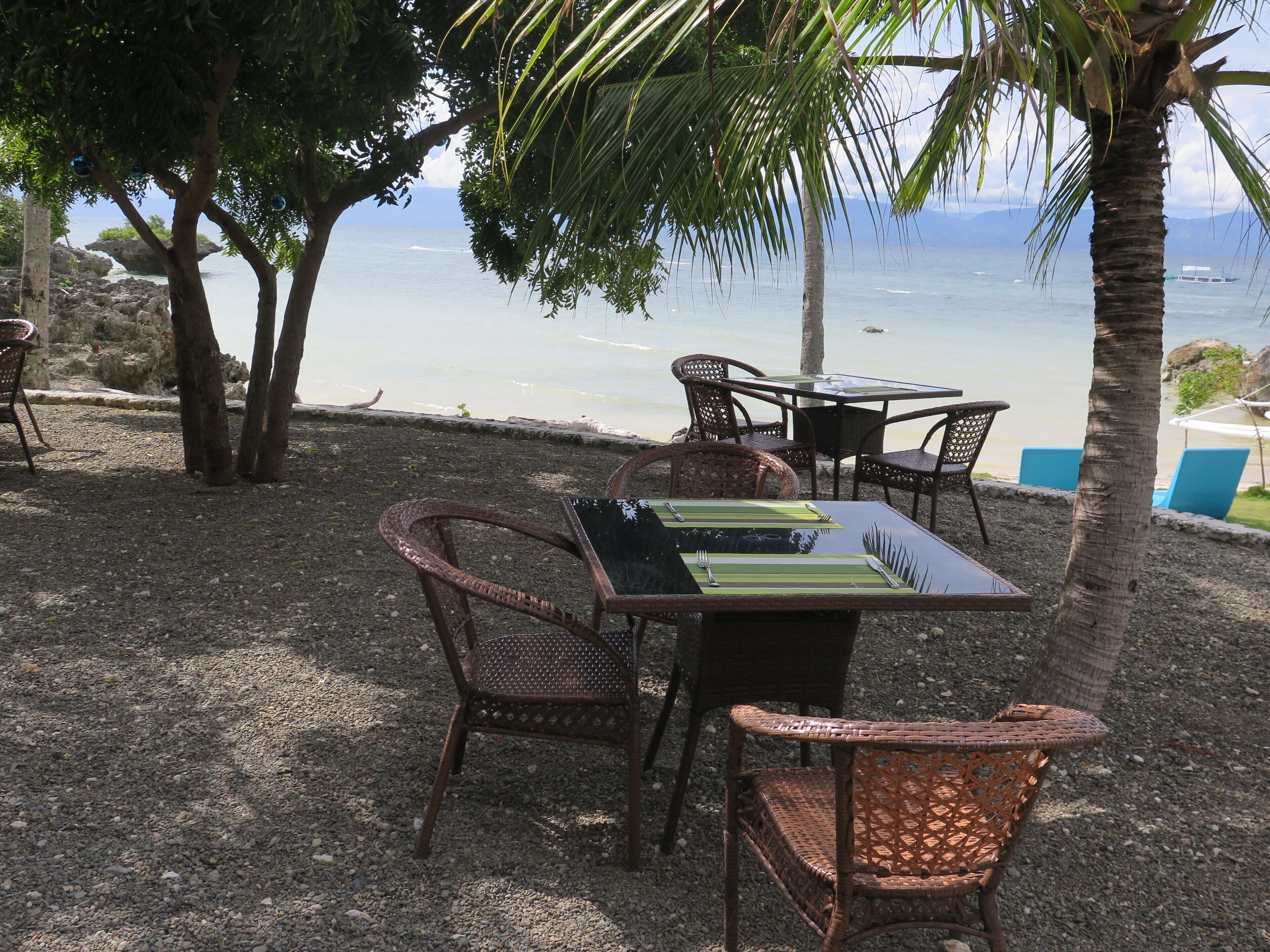 An outdoor dining area with wicker furniture and a table set for two, overlooking a body of water.