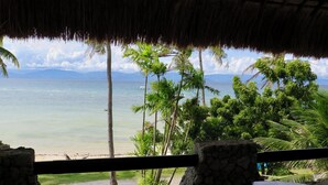 Estructura con techo de paja que domina una playa con palmeras y vista despejada al mar.