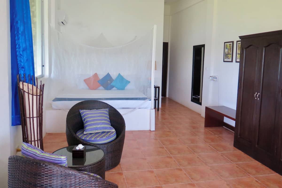 Una habitación con cama, una silla de mimbre, una mesita y un armario.