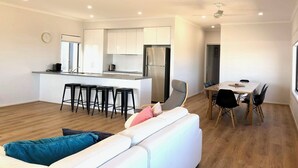 A modern kitchen with white cabinets, a stainless steel refrigerator, and a bar area with stools.