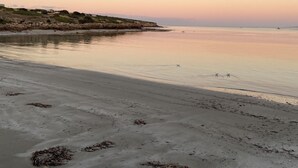 A beach with a calm sea, sandy shore, and distant hills.