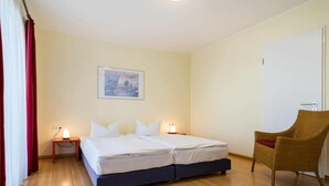 Habitación de hotel con una cama, una silla, una mesita de noche y un cuadro en la pared.