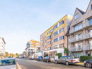 A street with multi-story buildings, parked cars, and a clear sky. - Apartment in Koksijde Near the Sea (Koksijde)