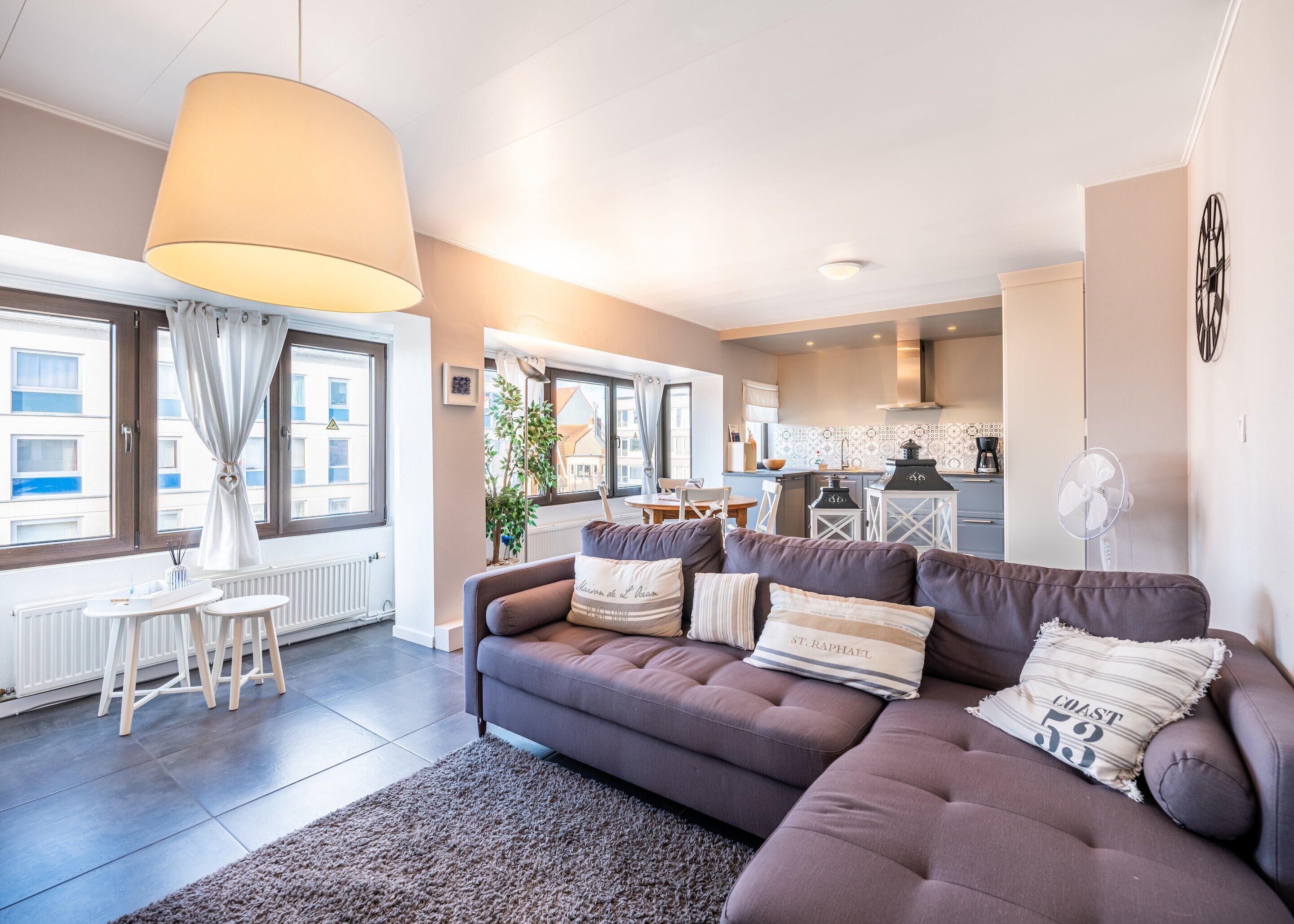 A modern living room with a sofa, a dining table, and a kitchen in the background.