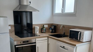 Una cucina compatta con piano cottura, forno, microonde, lavello e una finestra sopra il lavello.