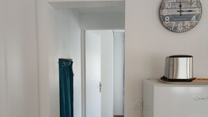 Un corridoio con un frigorifero bianco, una sveglia appesa al muro e una tenda color acquamarina.