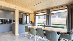 Una cocina moderna con armarios grises, una mesa de comedor de madera con sillas grises y un gran ventanal con cortinas.