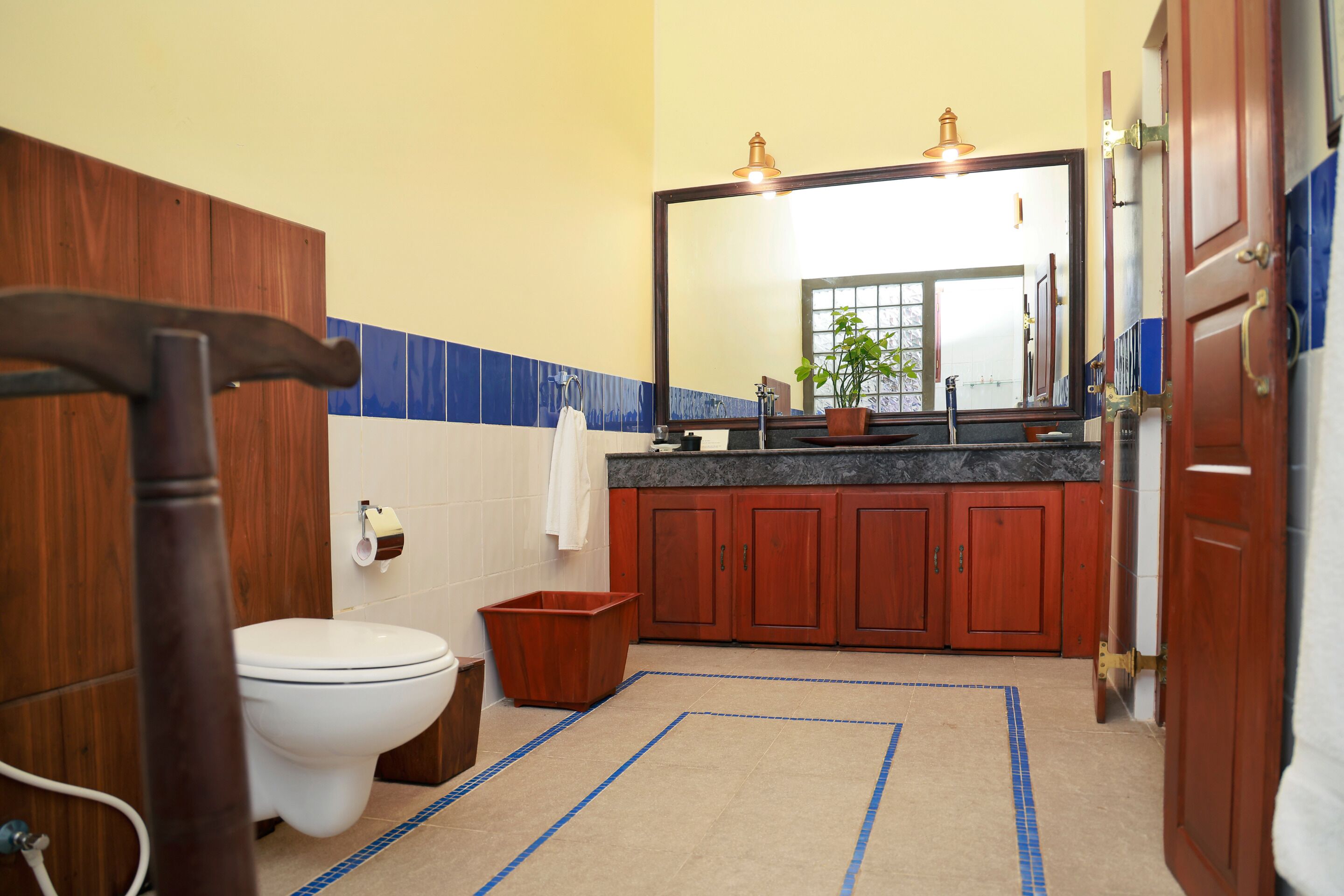 Une salle de bain avec un meuble-lavabo en bois, des toilettes blanches, un lavabo avec un miroir et une zone de douche carrelée de bleu.