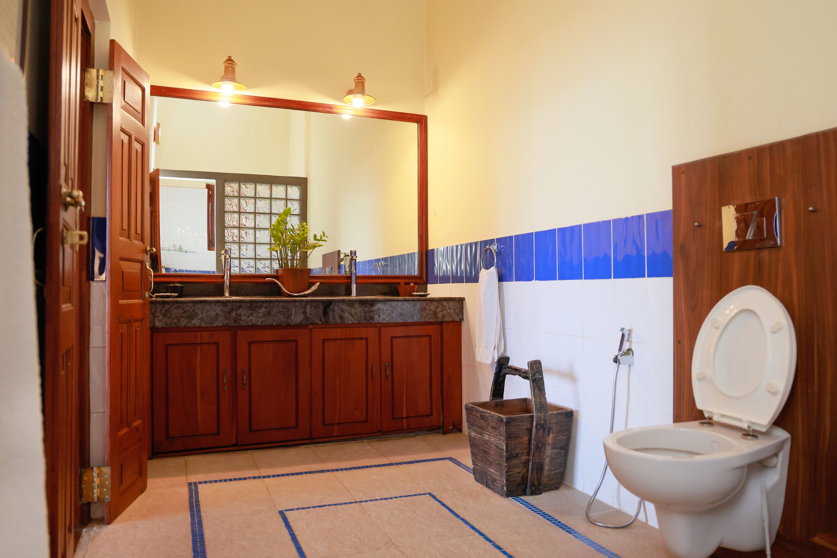 Une salle de bain avec des meubles en bois, un comptoir en marbre, un grand miroir, des toilettes blanches et un mur recouvert de carreaux bleus et blancs.