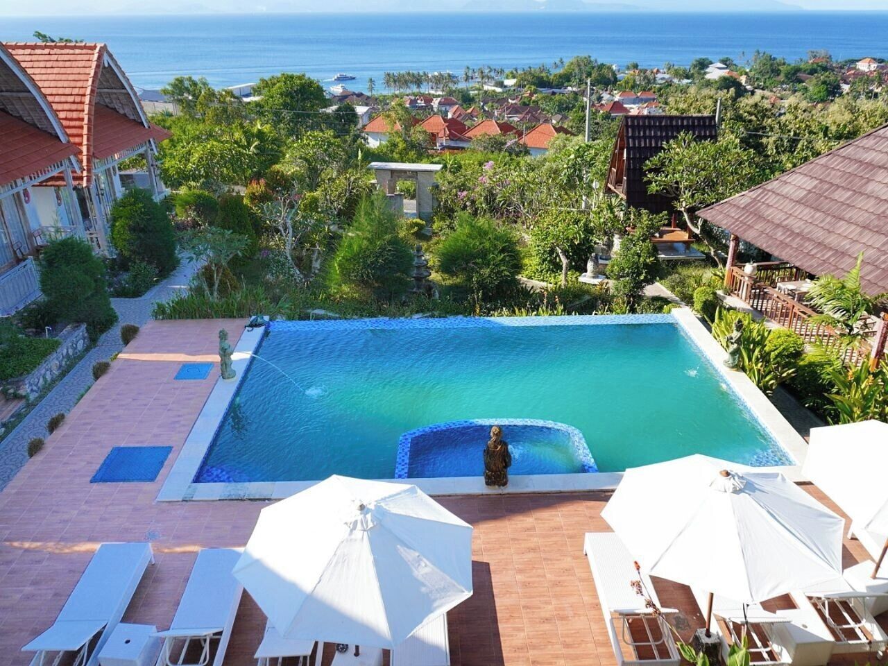Piscina con vista al océano, rodeada de vegetación y edificios.