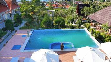 Piscina con vista al océano, rodeada de vegetación y edificios.