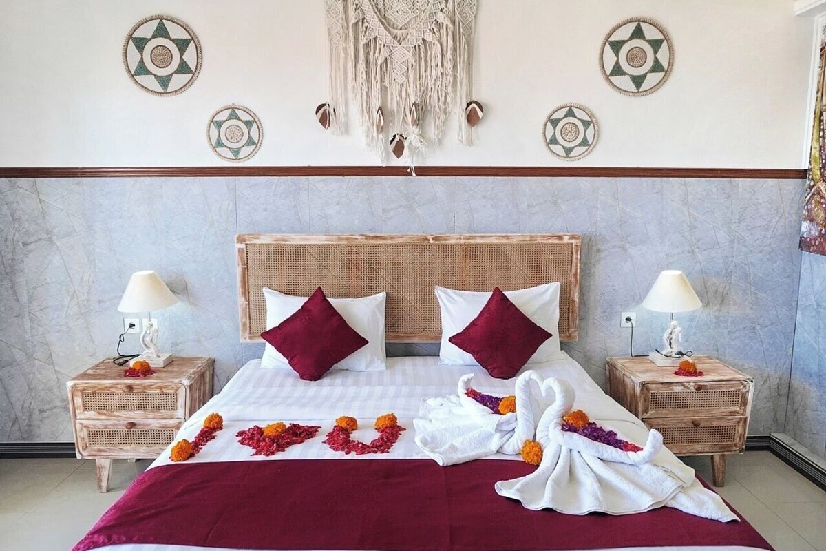Een bed met een rode sprei, twee kussens en een macramé wanddecoratie.