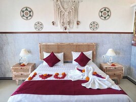 A bed with a red bedspread, two pillows, and a macrame wall hanging.