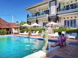 Una piscina con lettini e ombrelloni, una statua e un edificio con balconi.