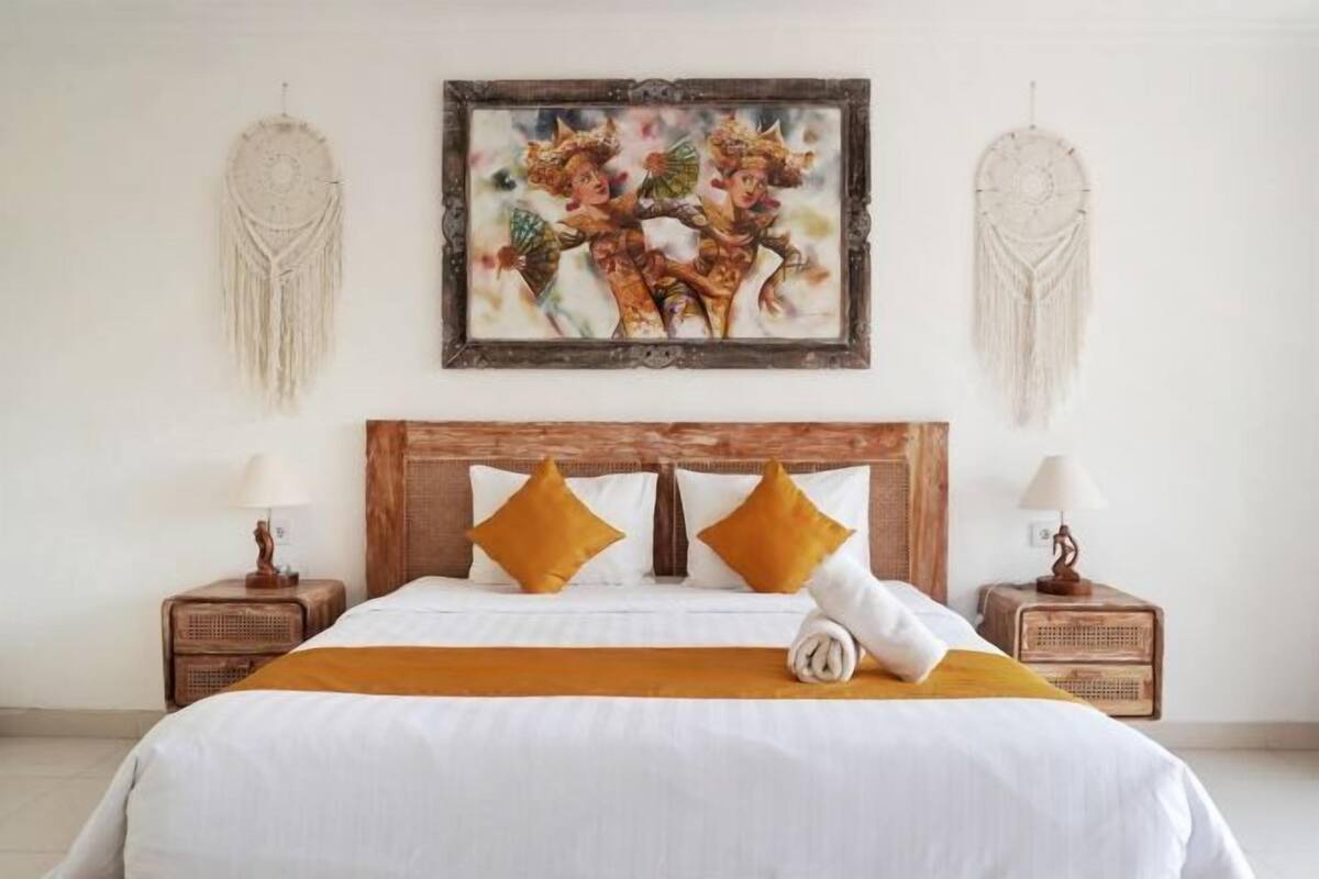 Habitación de hotel con cama, dos mesitas de noche, un cuadro y adornos de macramé en la pared.