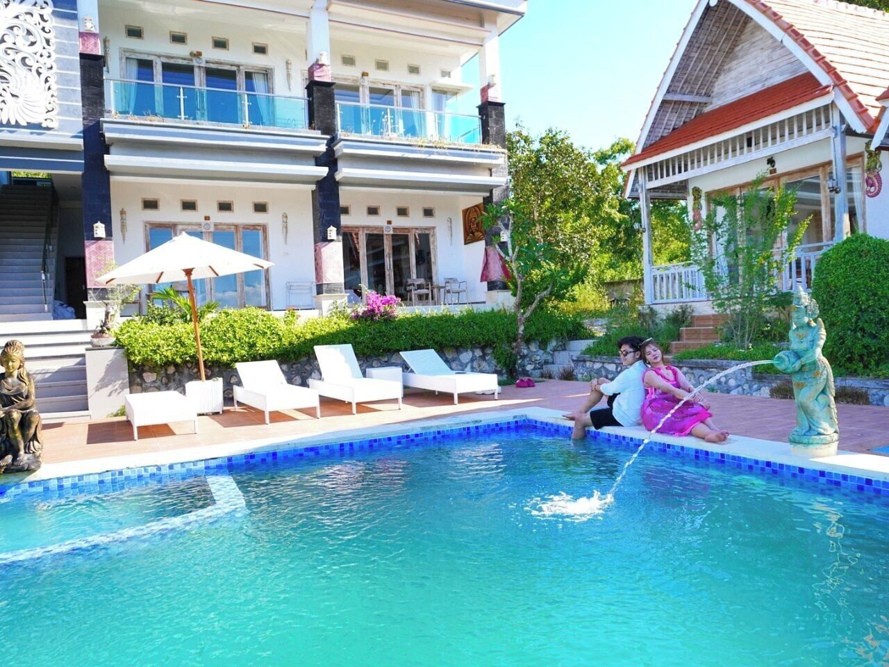 Une piscine avec des chaises longues, une statue et un bâtiment doté d’un balcon.