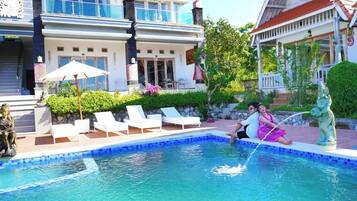 Une piscine avec des chaises longues, une statue et un bâtiment doté d’un balcon.