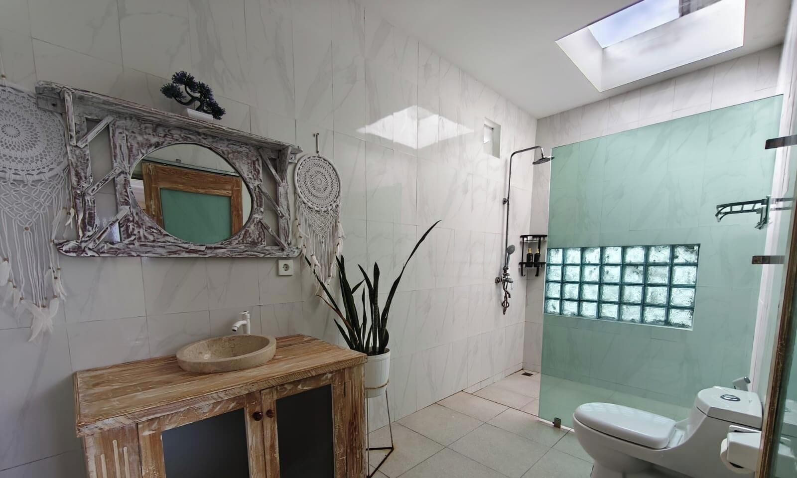Un baño moderno con un tocador de madera, un espejo grande, una cabina de ducha de vidrio y un inodoro.