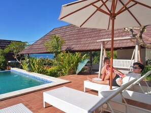 Un área junto a la piscina con sillones de descanso, un espacio de estar techado y vista al océano.