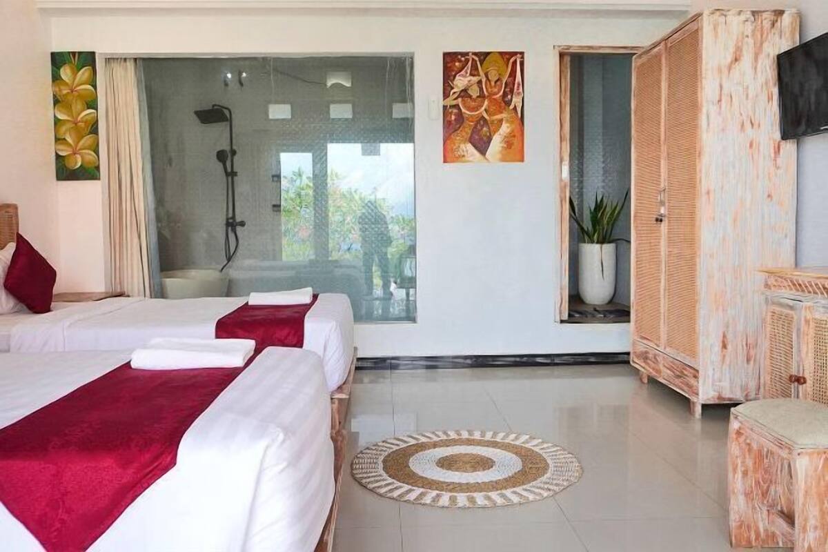 Habitación de hotel con dos camas, ducha, televisión y un ventanal con vistas.