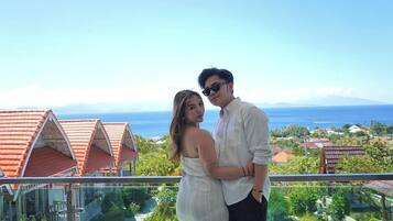 A couple standing by a pool with a view of the ocean and resort buildings.