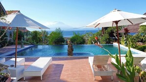 A pool with a statue, white lounge chairs, and umbrellas. - Darya Sea View (Penida Island)