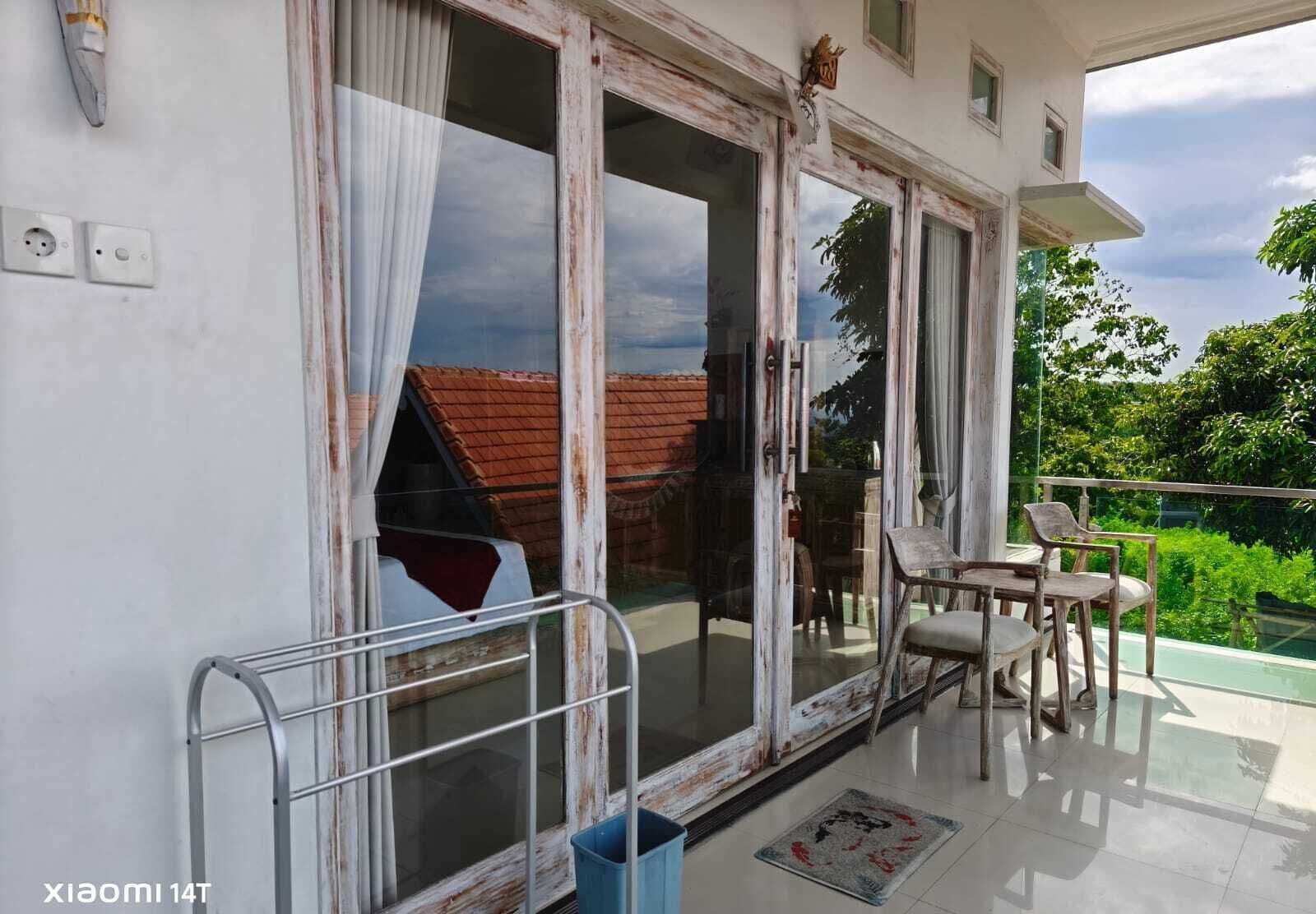 A balcony with a view of a red-roofed house, a metal chair, and a table.