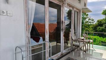 A balcony with a view of a red-roofed house, a metal chair, and a table.