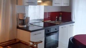 Eine kleine Küche mit weißen Schränken, einer roten Spritzschutzleiste, einer Kaffeemaschine und einem Esstisch.