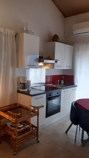 Une cuisine de taille réduite avec des meubles blancs, un crédence rouge, une machine à café et une table à manger.