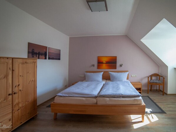A bedroom with a wooden bed, two bedside tables, a chair, and a large window. - Holiday Apartment Svantevit (Zingst)