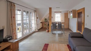 A spacious living room with a large window, a dining area, and a kitchen in the background.