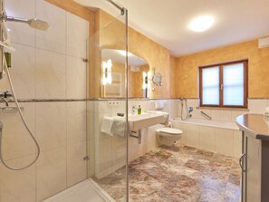 A modern bathroom with a glass-enclosed shower, a standalone bathtub, and a separate sink area. - Apartments Christiane (Oberammergau)