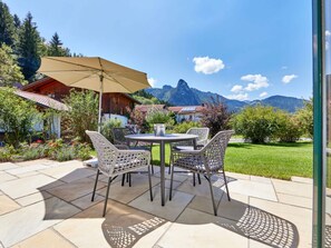 An outdoor patio with a table and chairs, a large umbrella, and a view of mountains. - Apartments Christiane (Oberammergau)