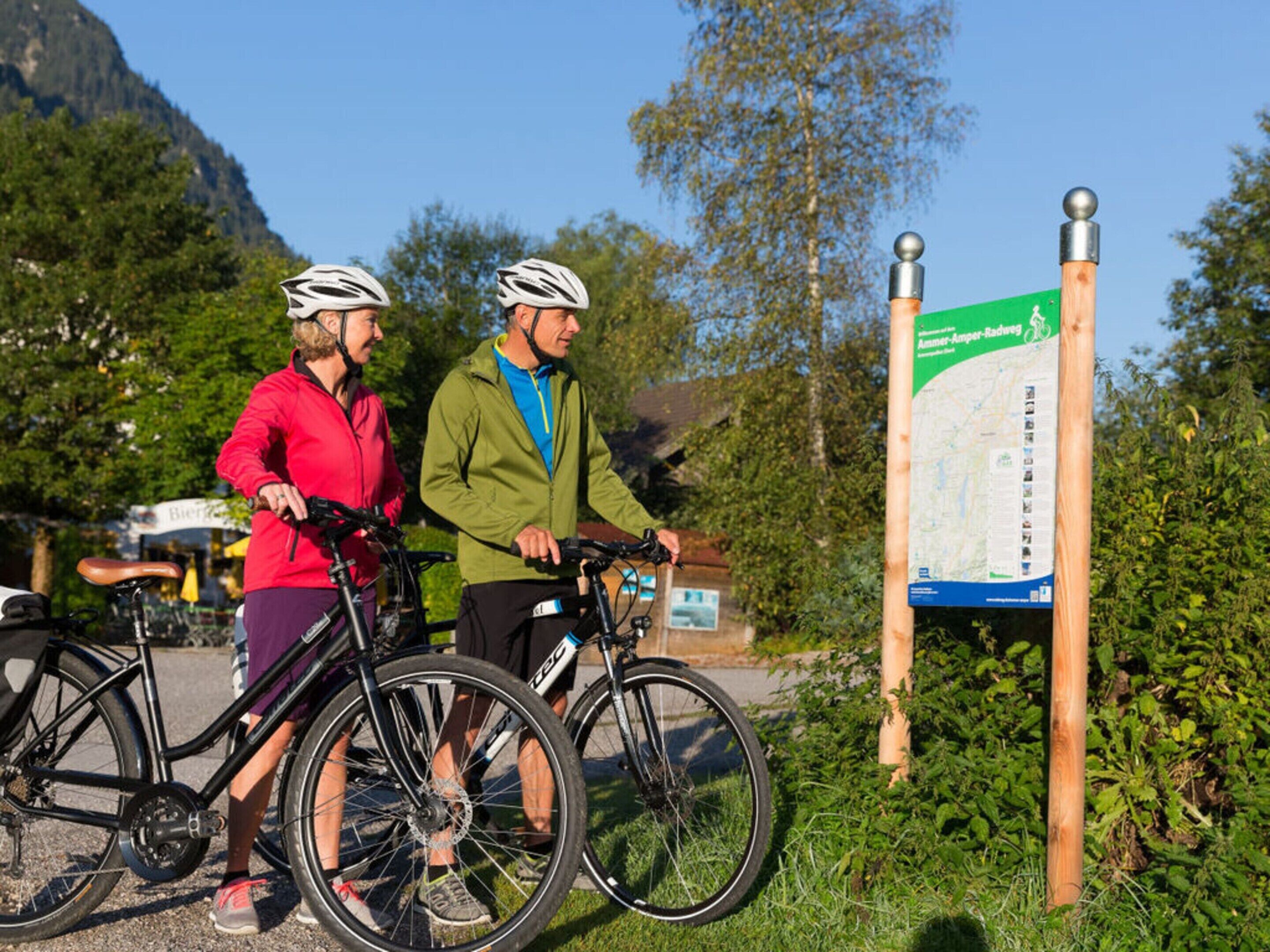 Zwei Personen mit Fahrrädern in der Nähe eines Wegweisers mit einer Karte.
