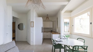 Et moderne køkken med hvide skabe, et spisebord med stole og en hængende lampe.