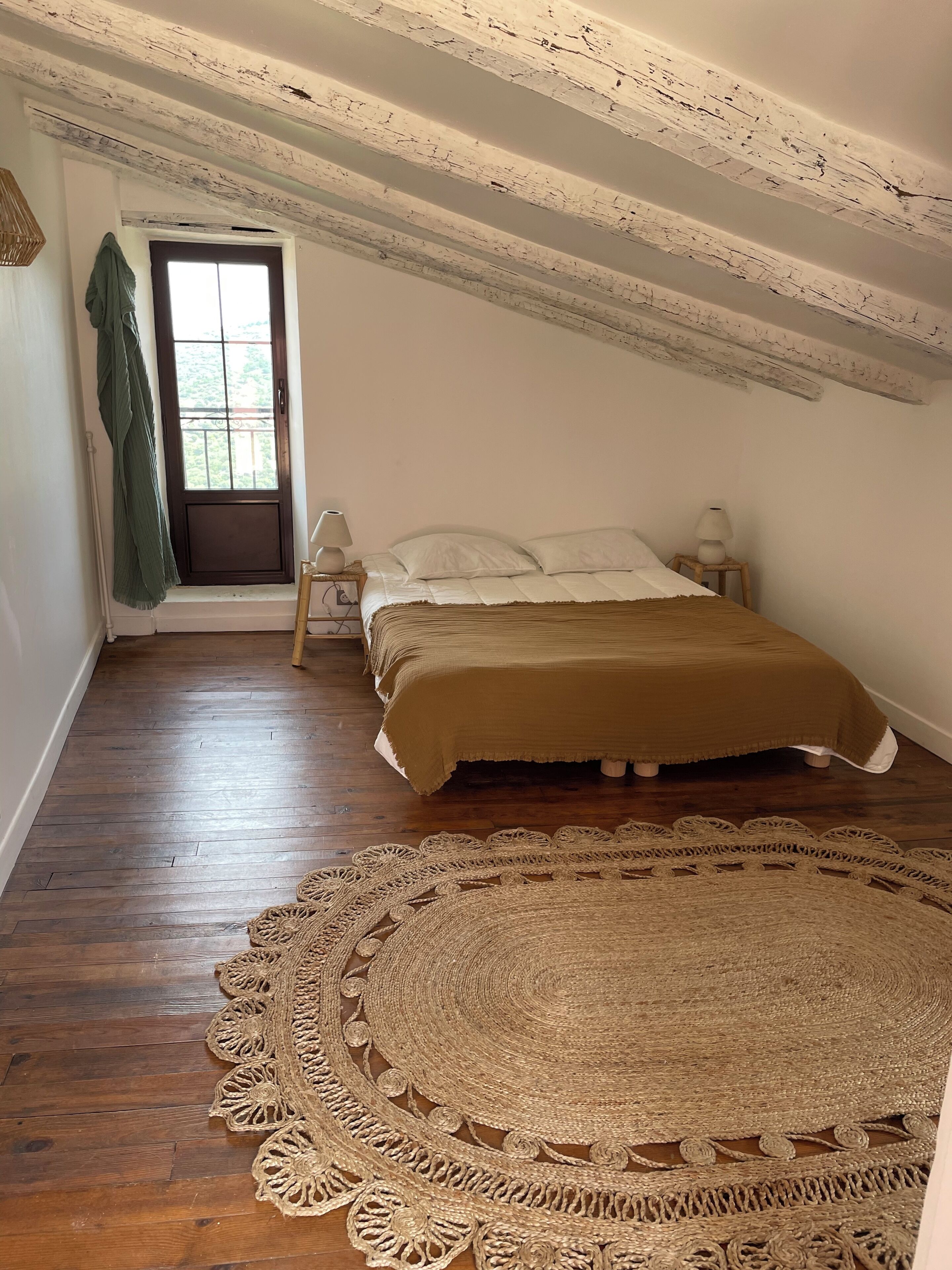 Une chambre avec un grand tapis aux motifs complexes, un lit recouvert d’une couverture marron, une fenêtre donnant sur un beau paysage et un plafond en bois.